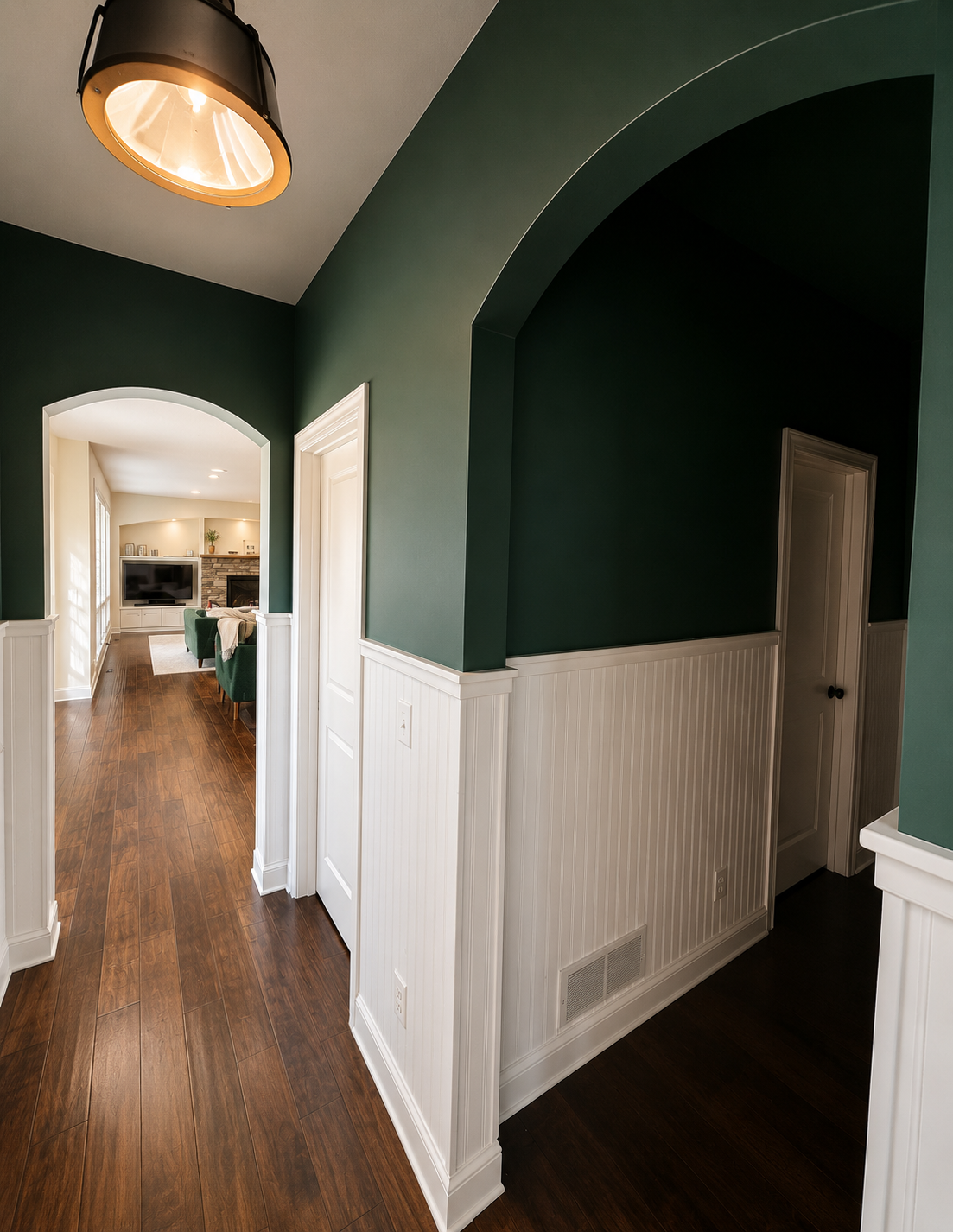 Hallway with deep green walls, white beadboard wainscoting, and arched openings